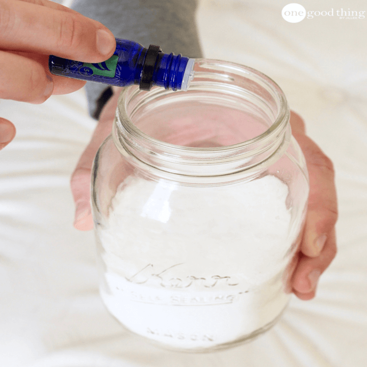 Hand sprinkling some essential oil into a mason jar of baking soda