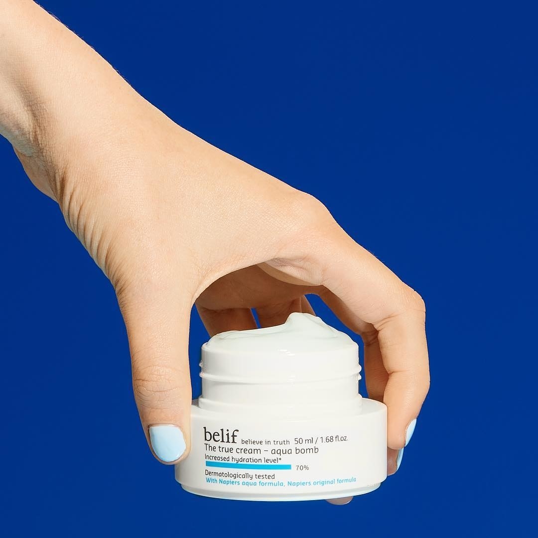 A hand holding the cream with lid off to show creamy texture 