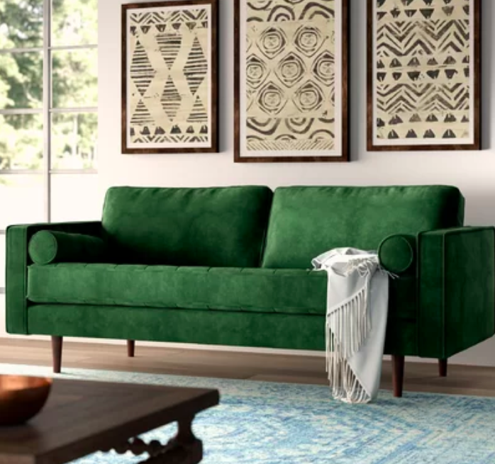 The green sofa with a white throw blanket hanging off of it