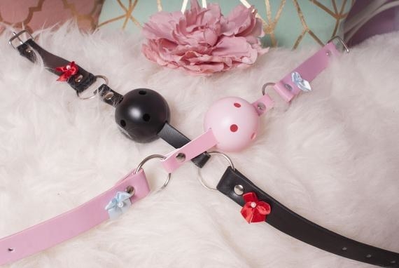 a pink and black ball gag with holes in it on a faux fur background 