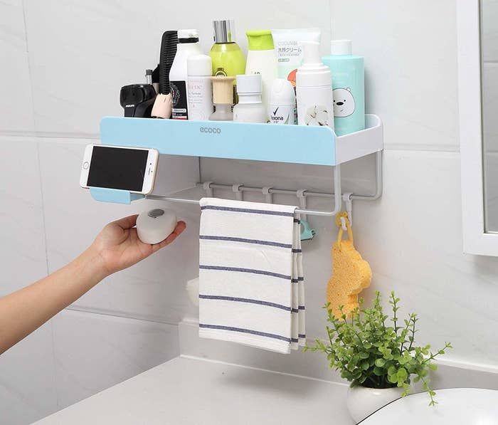 wall organizer with ta op bin filled with products, hooks below and a towel rod in the front with a place to set a phone 