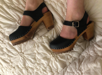 A different reviewer wearing the clogs in black, showing off the stapled-style leather top, wooden heel, and buckle straps at the ankle