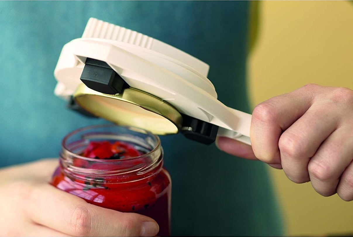 hand holding jar opener&#x27;s handle and it&#x27;s round top removing a lid