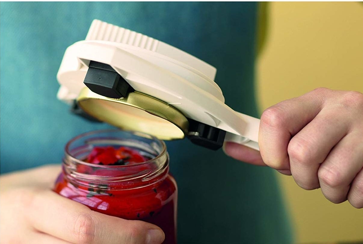 hand holding jar opener&#x27;s handle and it&#x27;s round top removing a lid