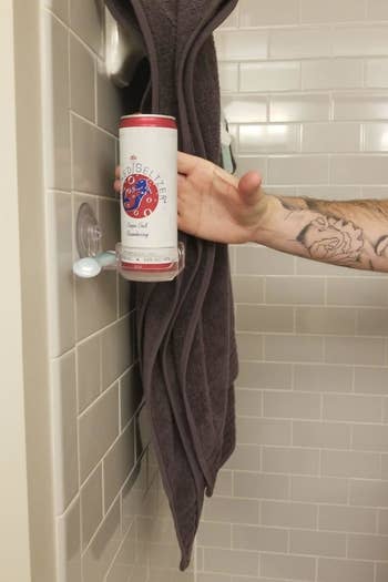 reviewer grabbing can from holder on tile shower wall