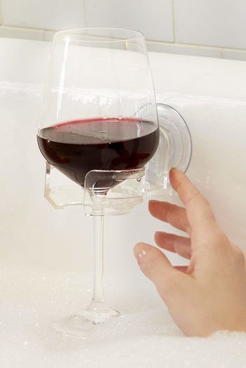 hand grabbing wine glass in holder attached to bathtub wall
