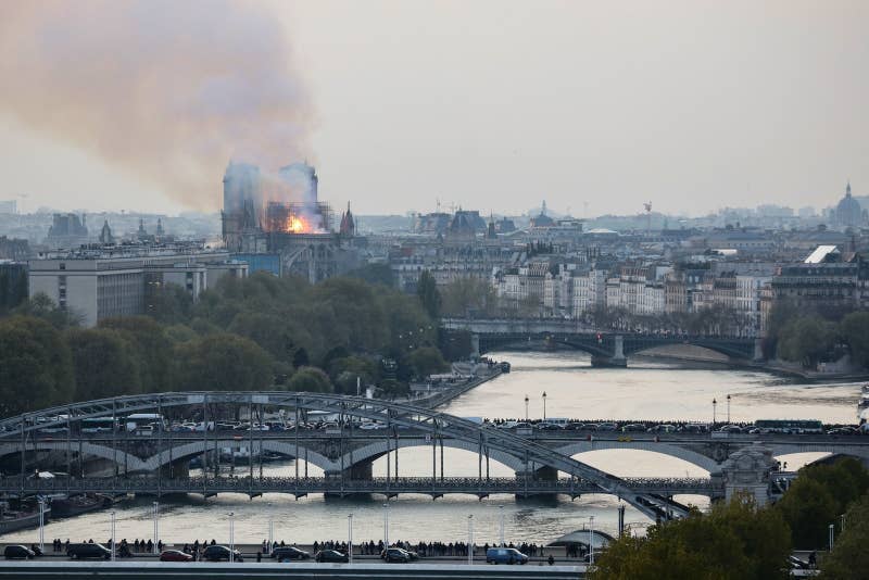 Bystanders stand on bridges across the River Seine as they watch flames and smoke billowing from the roof of Notre-Dame Cathedral in Paris on April 15, 2019. - A fire broke out at the landmark Notre-Dame Cathedral in central Paris, potentially involving renovation works being carried out at the site, the fire service said.Images posted on social media showed flames and huge clouds of smoke billowing above the roof of the gothic cathedral, the most visited historic monument in Europe. (Photo by LUDOVIC MARIN / AFP) (Photo credit should read LUDOVIC MARIN/AFP/Getty Images)