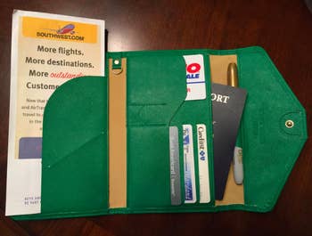 A reviewer's green wallet with several pockets holding plane tickets, cards, and a passport