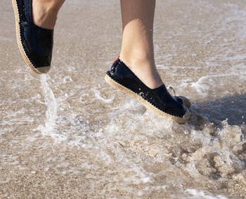 Model wearing the espadrilles while jumping in the water at the beach