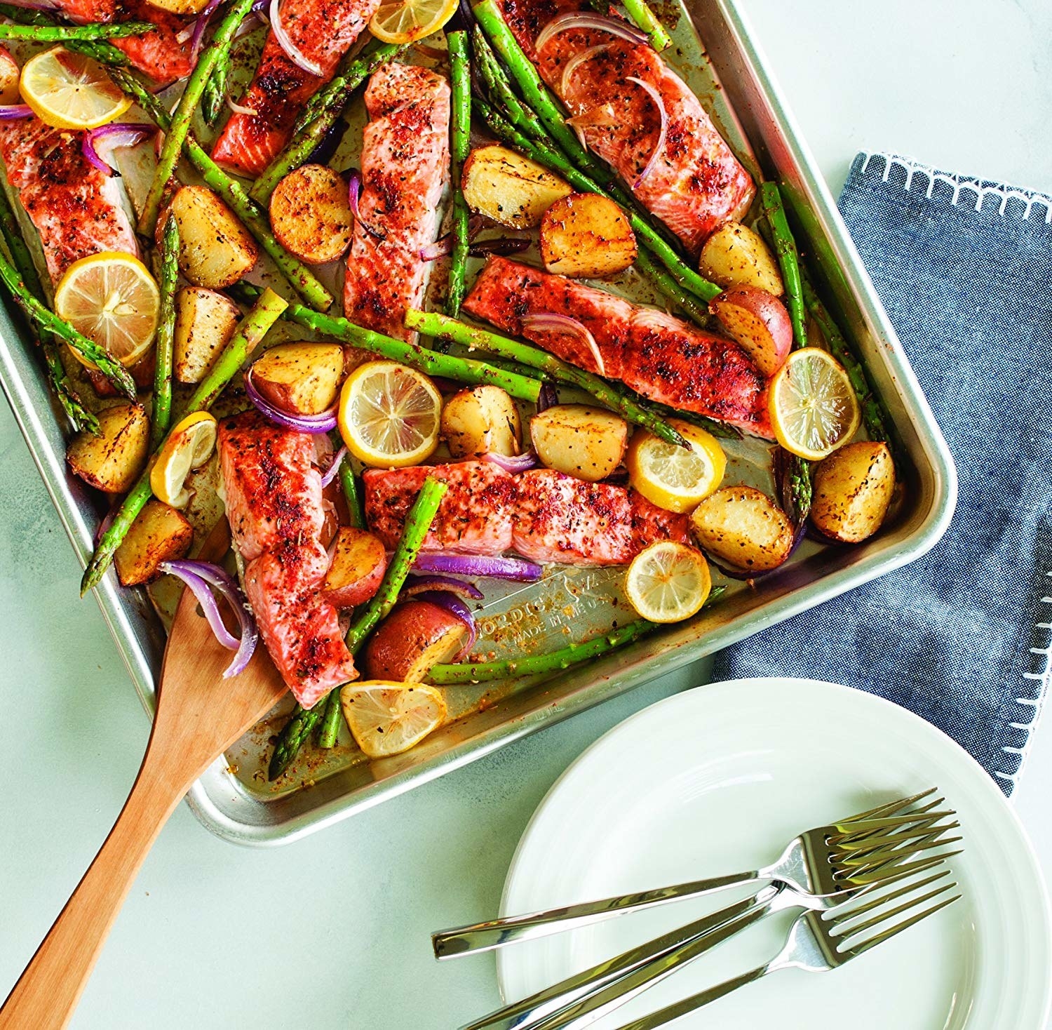A sheet pan with salmon, potatoes, lemon slices, and asparagus on it