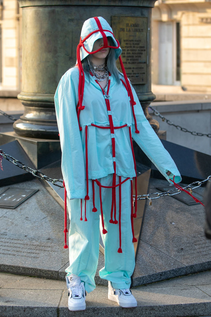 Billie com um conjunto azul e cordas vermelhas penduradas