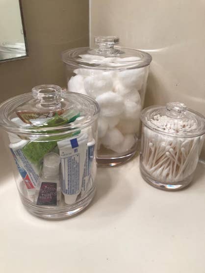 Reviewer photo of three clear plastic jars filled with various toiletries and placed on bathroom sink