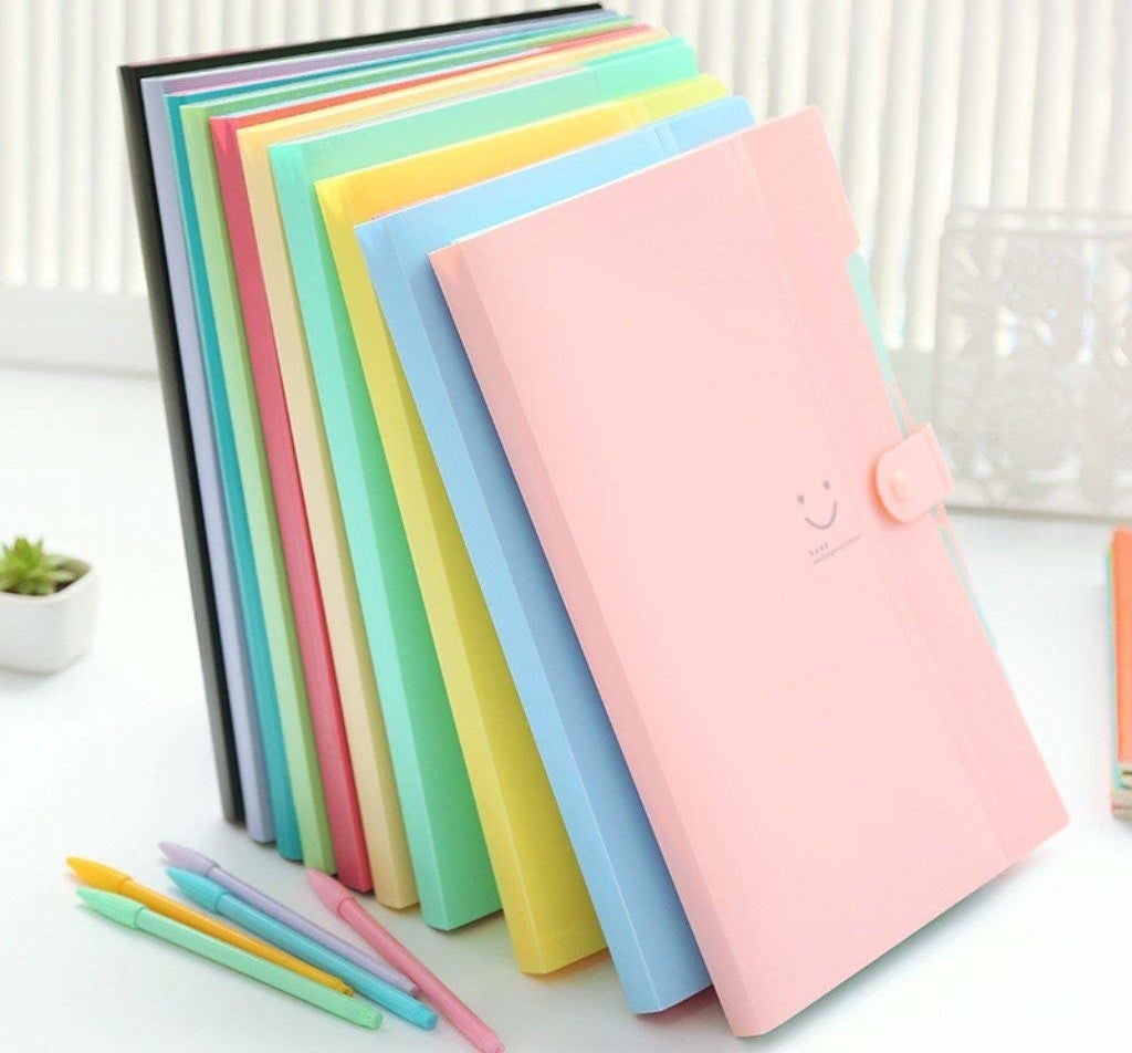 A stack of file folders in varying pastel-like colors that have a little smiley face on the front 