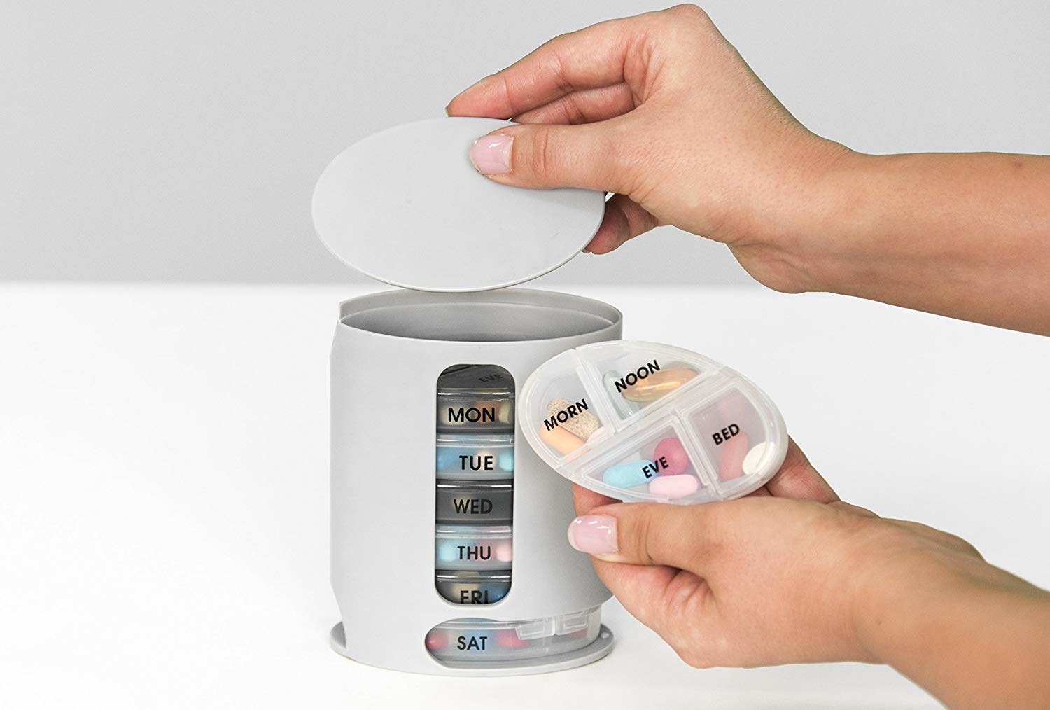 A person&#x27;s hands taking out one of the pill trays from the pill keeper. The pill tray has four different sections — morning, noon, evening, and bed