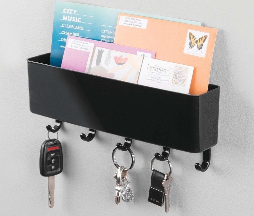 A black organizer hanging on the wall filled with envelopes, featuring five hooks on the bottom holding onto keys