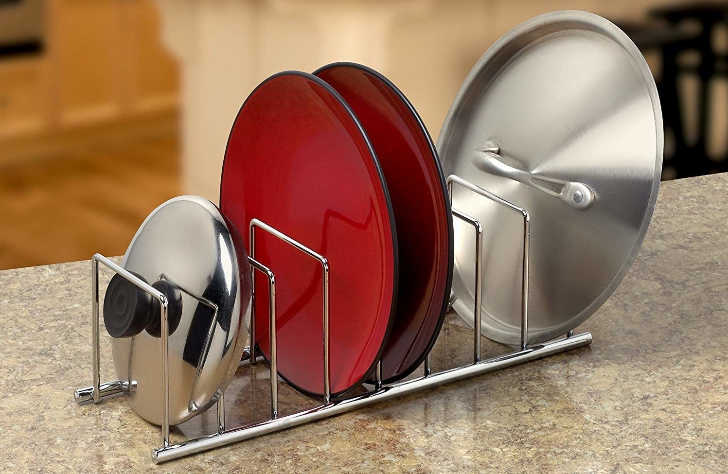 A metal rack holding a pot lid, two plates, and a pan lid of varying sizes, with four more free compartments for holding kitchenware