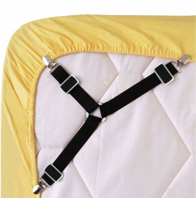 The black clip-on straps, which look like a three-pronged suspender, securing the edges of a fitted sheet around the bottom of a mattress