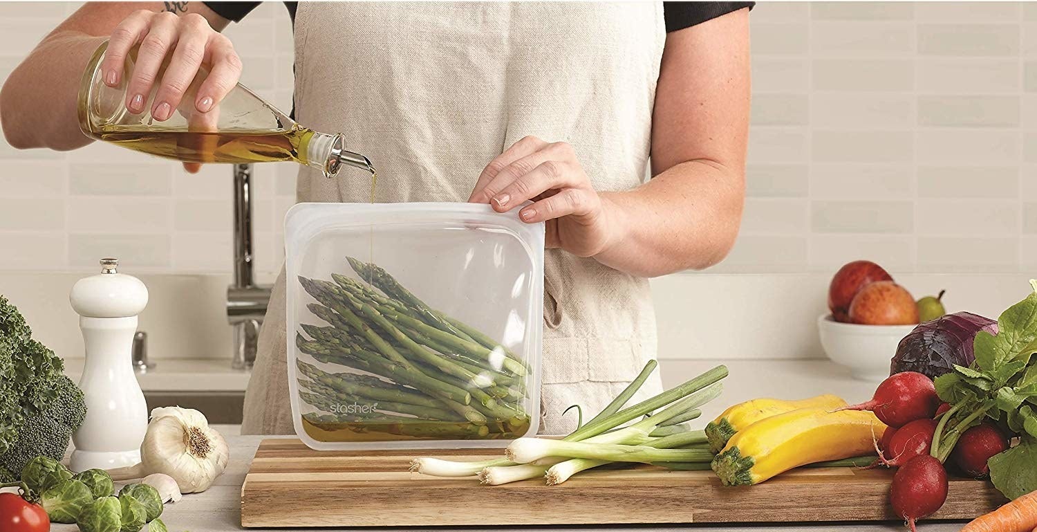 person pouring olive oil into stasher bag holding asparagus 