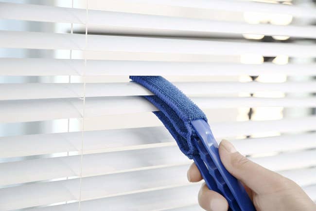person cleaning blinds with duster