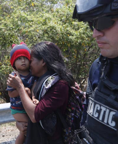 A Central American migrant woman and her son walk with a Mexican Federal Police agent as they are taken into custody.