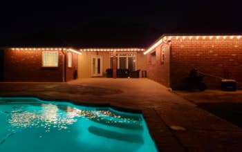 reviewer pic of the string lights along roofline in back of house by a pool patio area