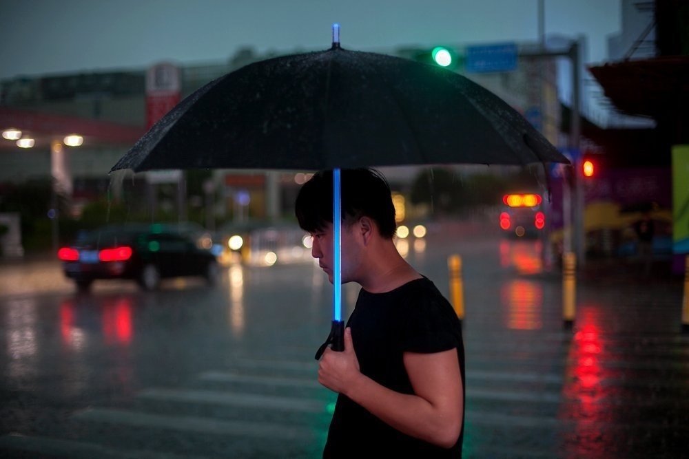 A person holding the umbrella, which has a shaft that glows like a lightsaber 
