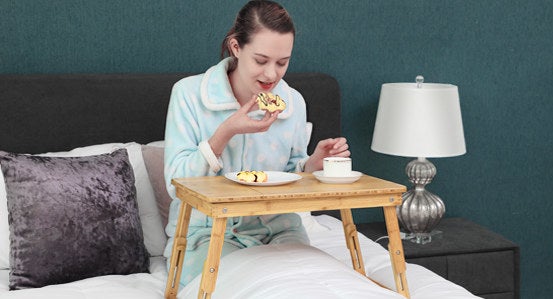 person using the table-like wood lap desk in bed to hold a breakfast plate, cup of coffee