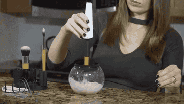 a gif of a model using the brush spinner and bowl to clean a makeup brush