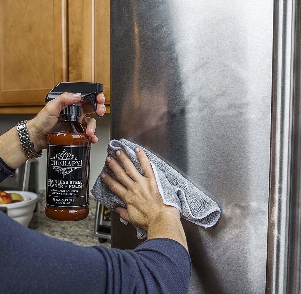 A model holding a spray bottle of the cleaner with one hand, and with the other, wiping off a dirty fridge so you clearly see how quickly and thoroughly the cleaner works