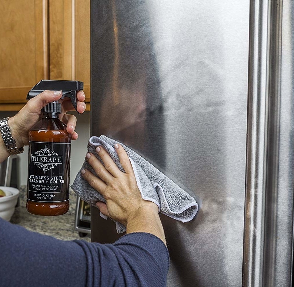 A model holding a spray bottle of the cleaner with one hand, and with the other, wiping off a dirty fridge so you clearly see how quickly and thoroughly the cleaner works