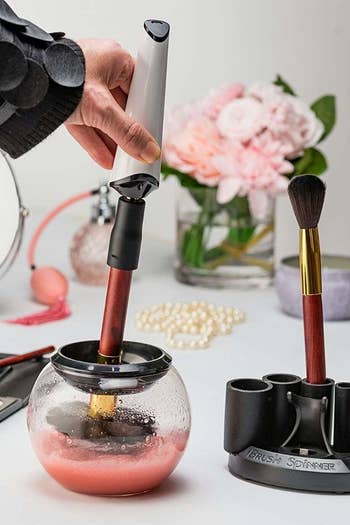 A person dipping a makeup brush attached to the brush spinner into a round glass bowl for washing
