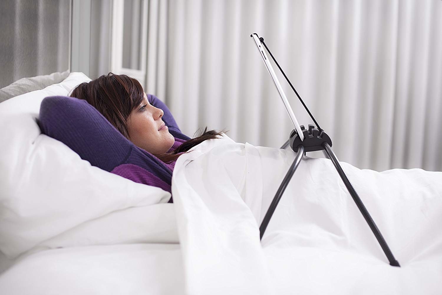 person lying in bed with the stand over them holding a tablet