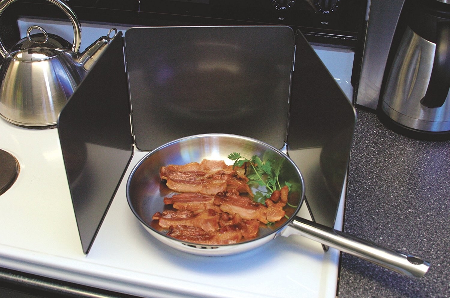 A pan full of bacon on a stove top with the three-wall splatter guard around it