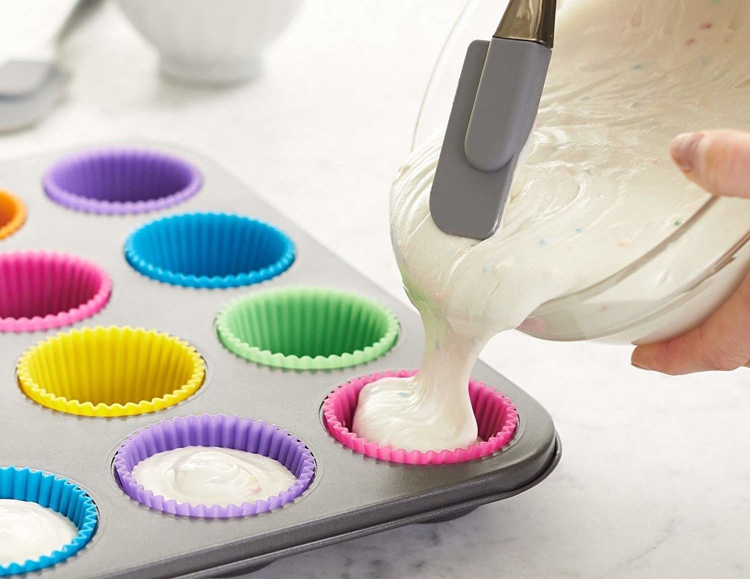 A person pouring batter into the colorful silicone baking cups