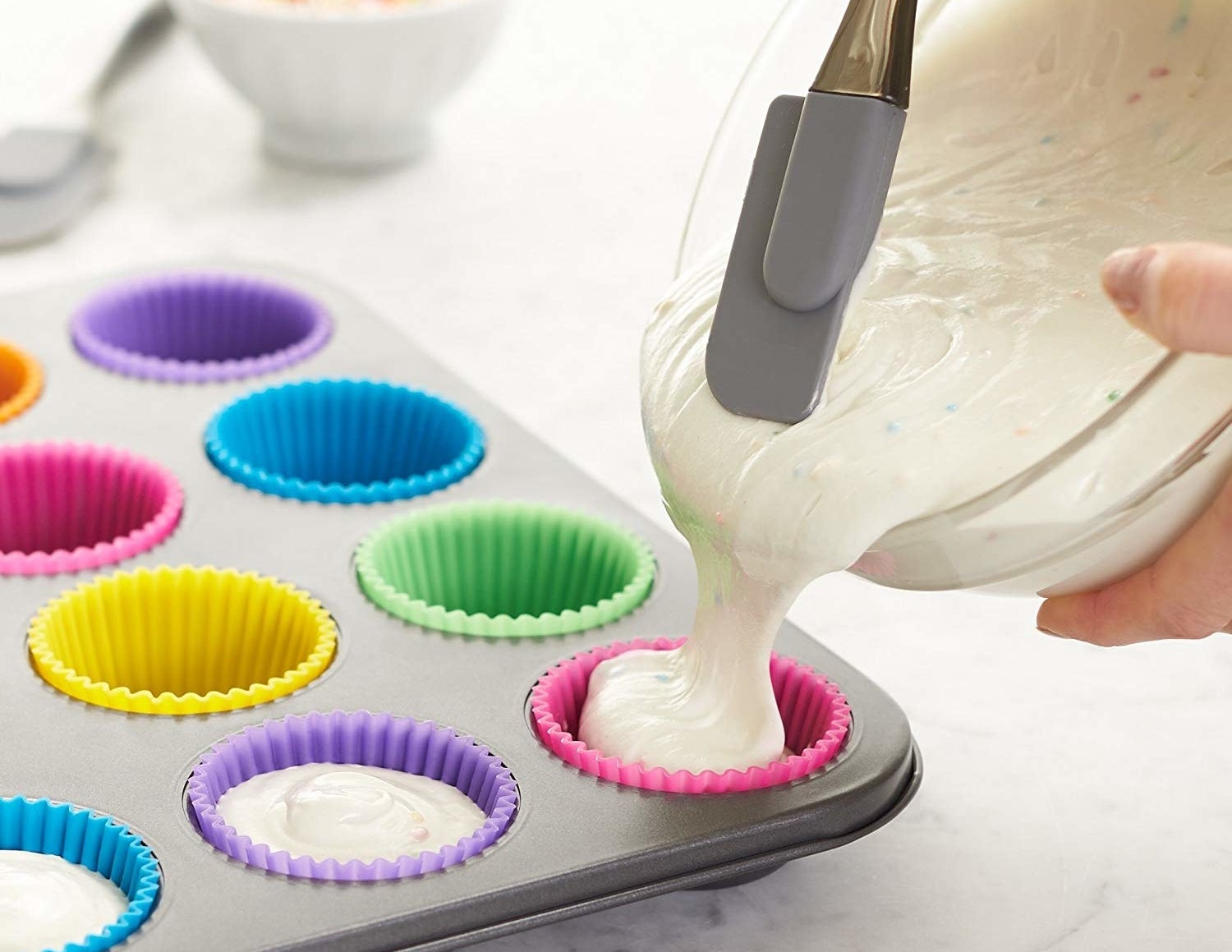 A person pouring batter into the colorful silicone baking cups