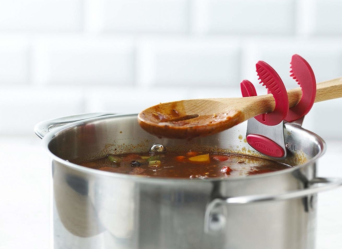 The clips holding a wooden spoon over a pot of sauce or soup