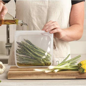 Model pouring oil into upright Stasher bag filled with asparagus