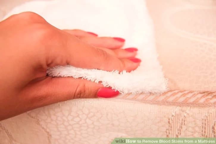 A hand blots a mattress with a towel