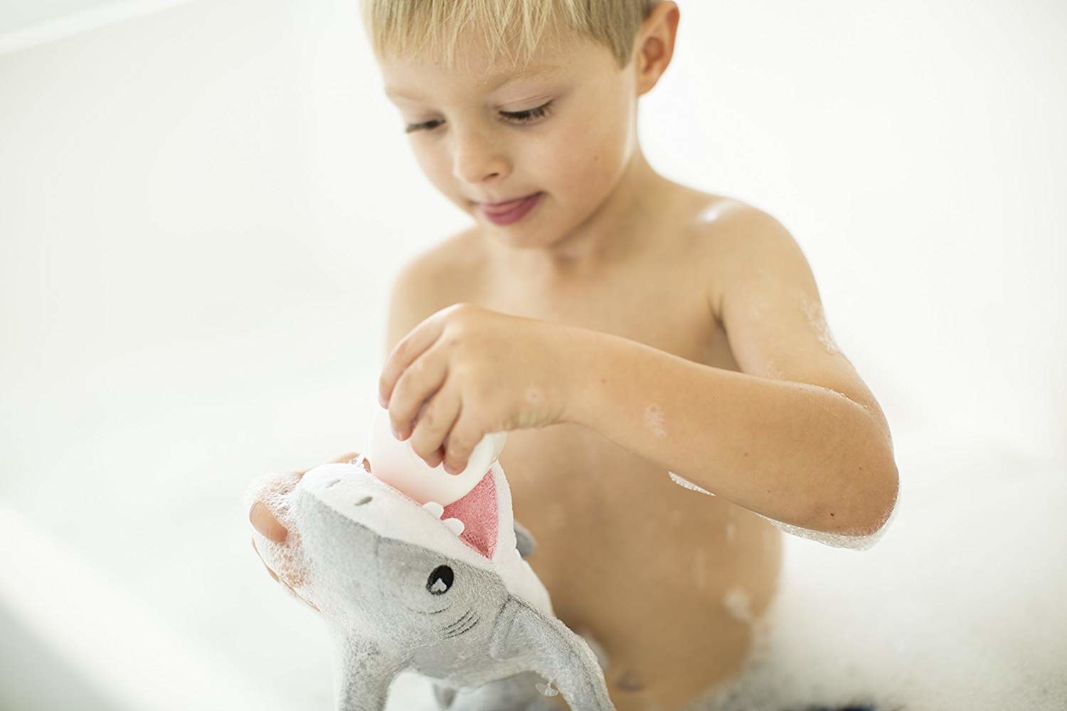 A little kid playing with the shark sponge in the bath