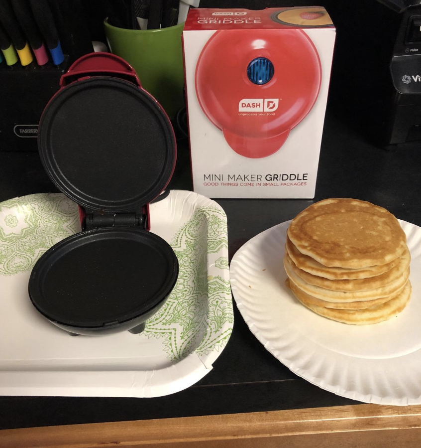 A reviewer photo of the Dash mini griddle open next to a stack of pancakes 