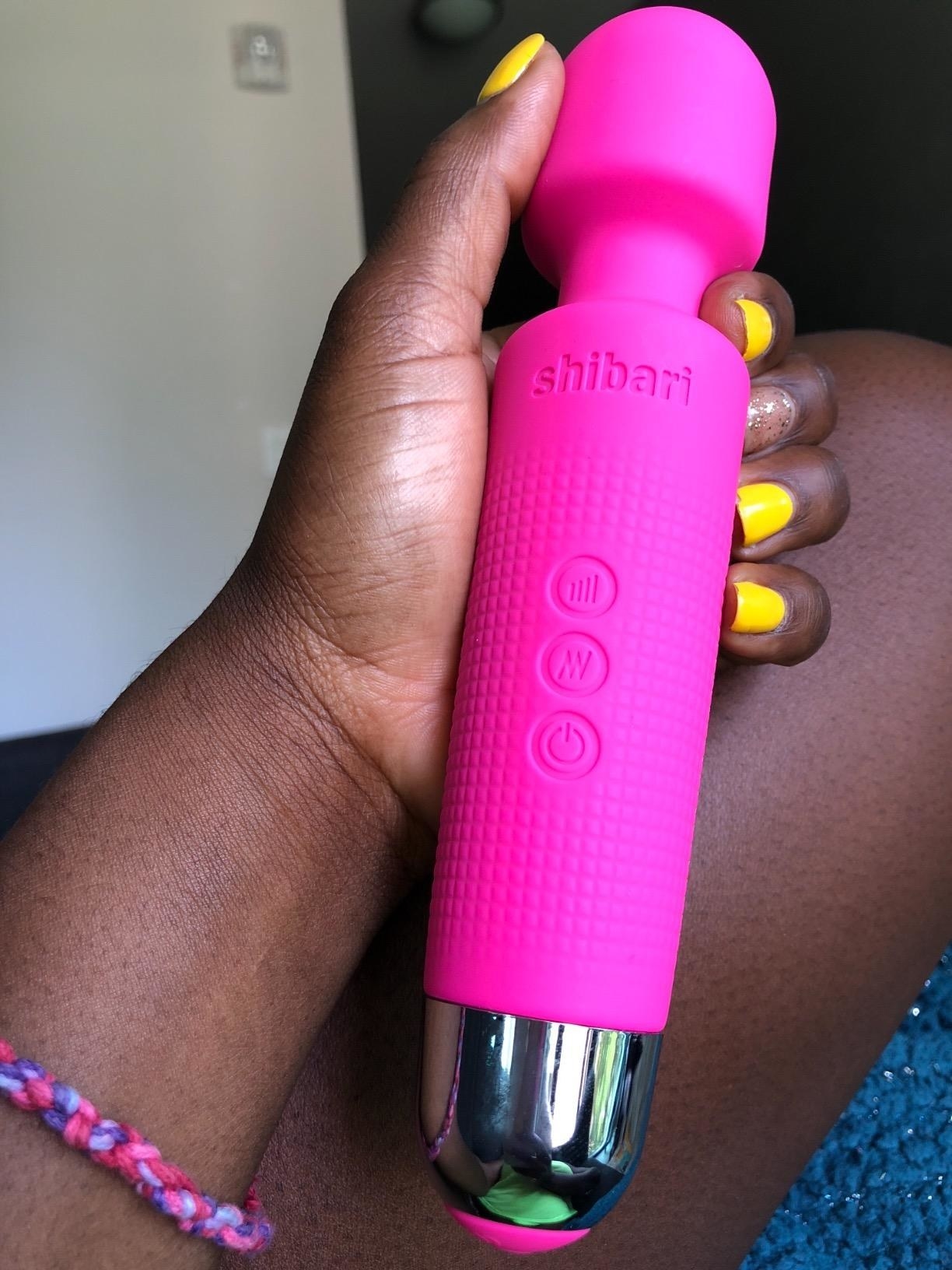 A reviewer holding the forearm-sized dildo. It is covered in silicone, has three buttons, and a rounded end with a small tapered neck. 