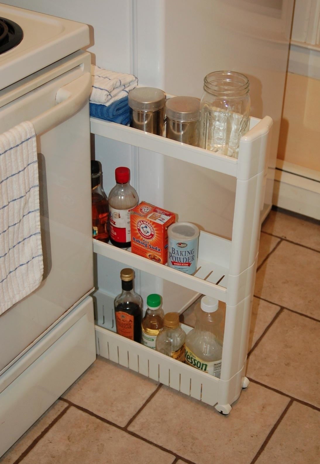 Reviewer photo of the storage tower with three shelves filled with food and cooking ingredients between a stove and fridge