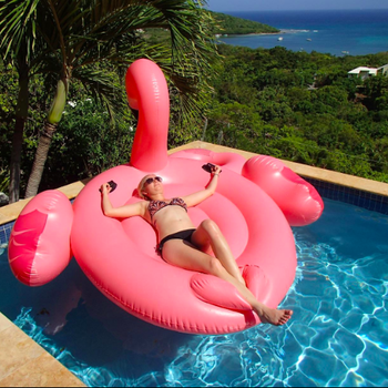 A reviewer lying face up on the massive flamingo in a pool, with their hands on the handles