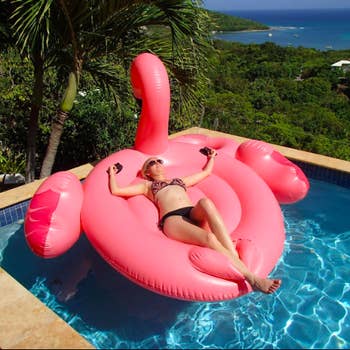 A reviewer lying face up on the massive flamingo in a pool, with their hands on the handles