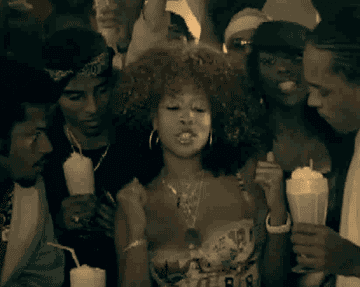 Kelis dancing while a bunch of men holding milkshakes crowd around her
