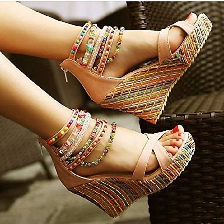 a model wearing the beaded wedge sandals in a light tan color with a zip-up back and beading around the ankles