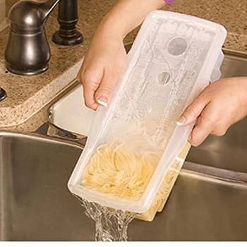 A model's hand holding the pasta cooker and pouring the water out into the sink with cooked pasta inside