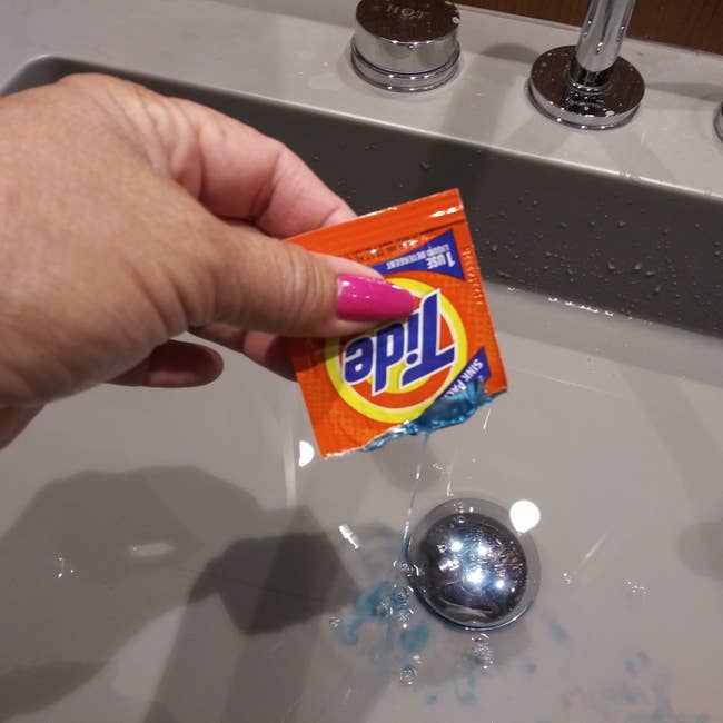 person dumping packet of clothes detergent in a sink full of water
