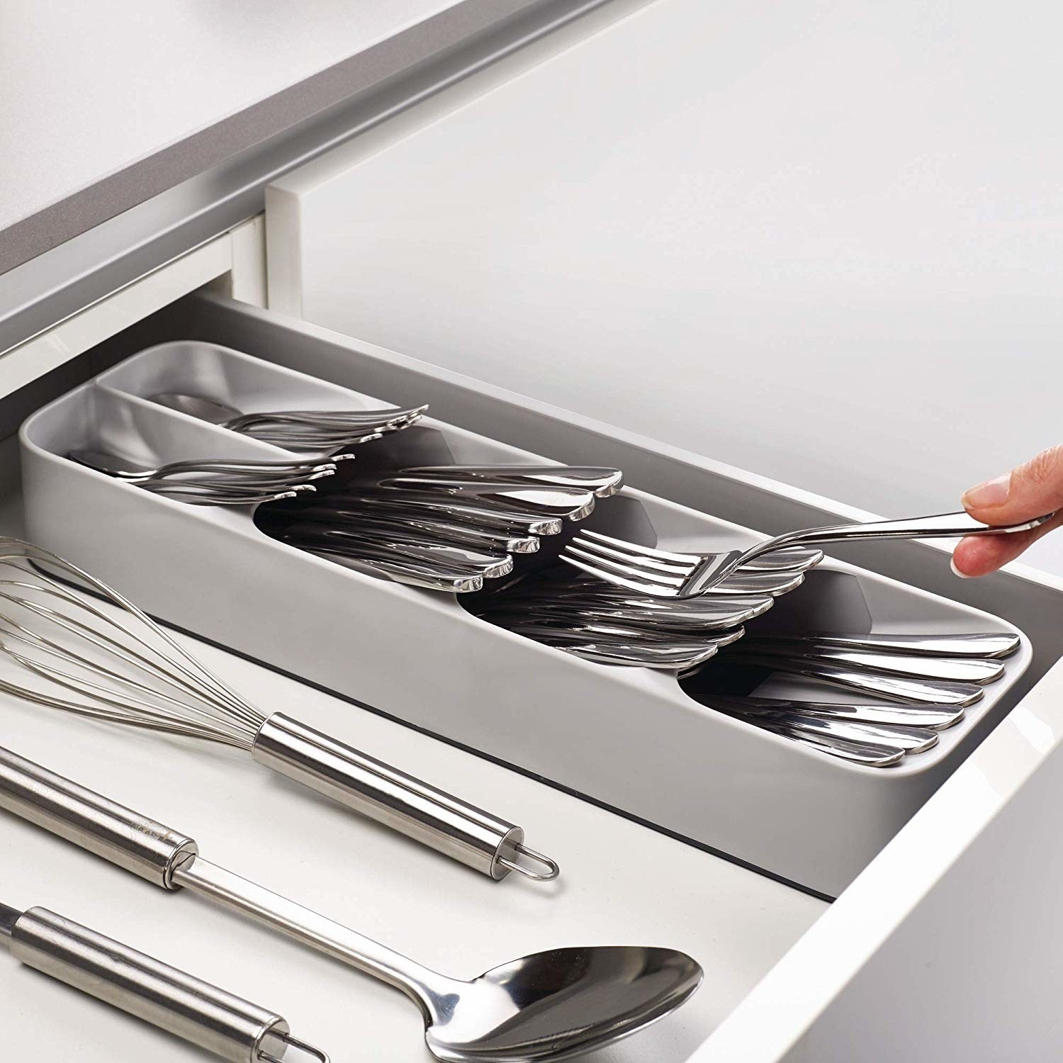 A hand putting a fork into the rectangular organizer; it has four slots at diagonal angles, one stacked on top of the next, with wide-mouth openings 