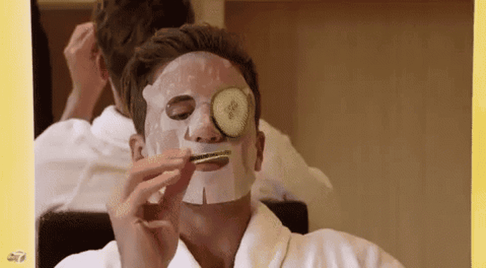 Gif of a man eating a cucumber while wearing a face mask and robe at a spa 